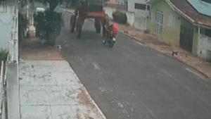 Imagem colorida mostra uma moto, com duas pessoas, em uma rua, e uma máquina agrícola vindo no sentido oposto antes de um acidente acontecer.